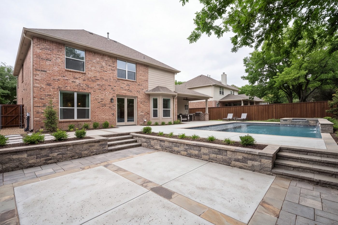Back yard with a stone and concrete patio, retaining wall and pool deck, house in frame